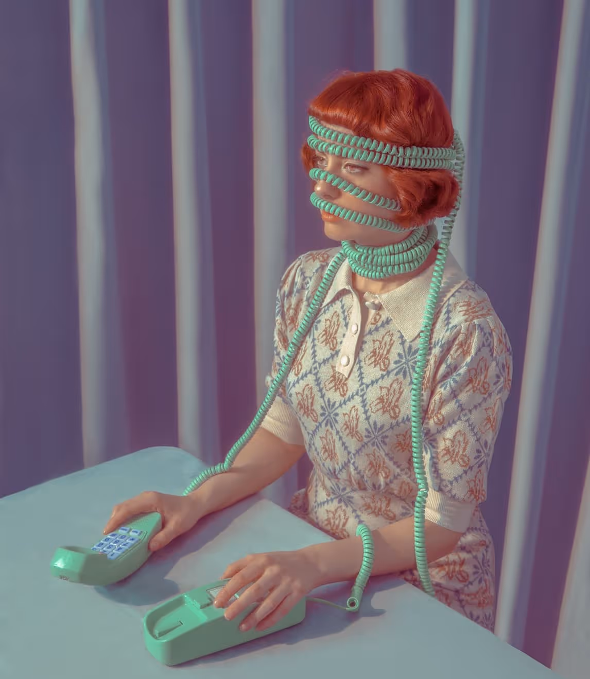 Woman with red hair wrapped in coiled turquoise telephone cords around her head, face, and neck against a purple curtain backdrop.