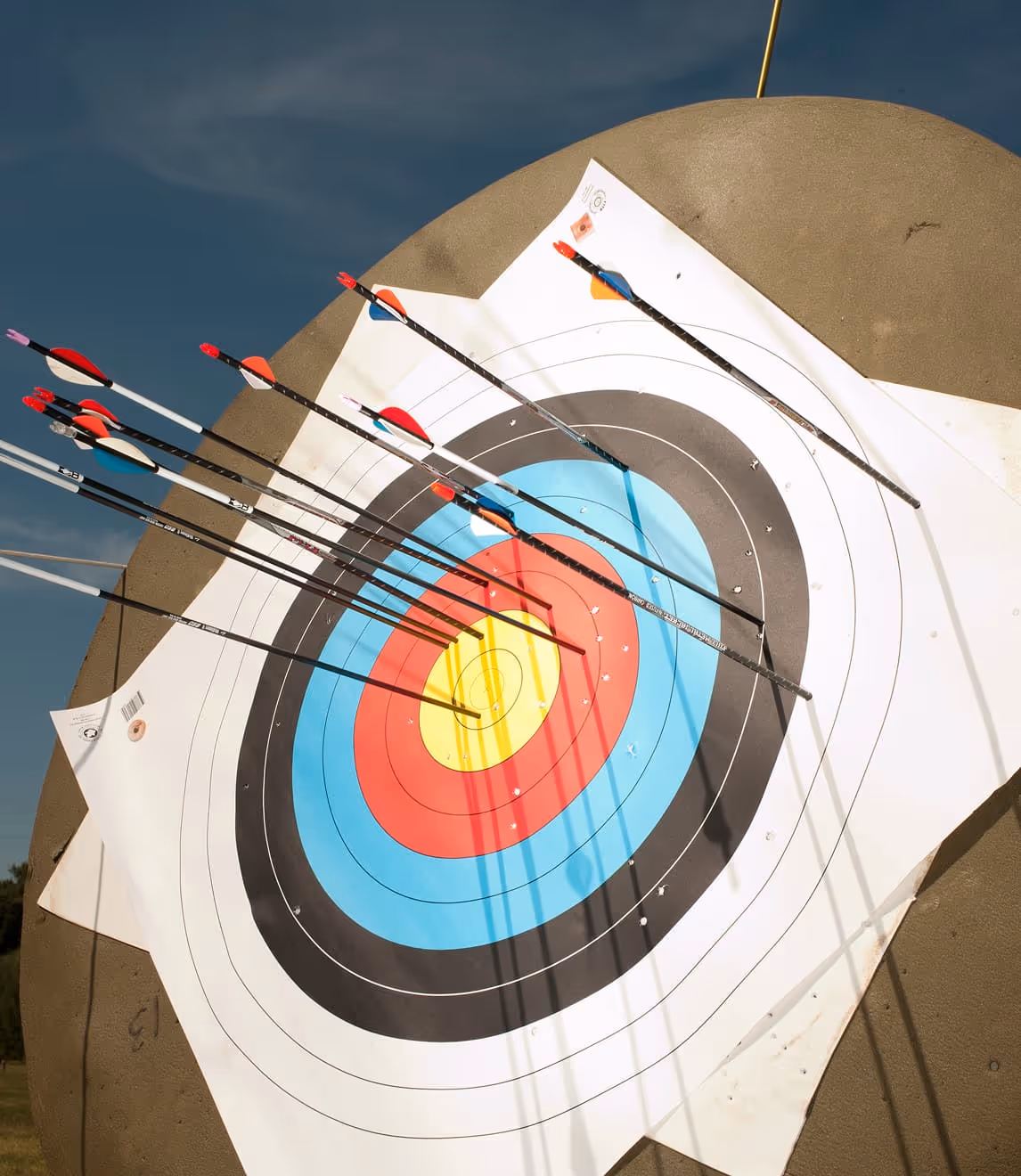 Archery target with multiple arrows clustered around the bullseye in an outdoor setting.