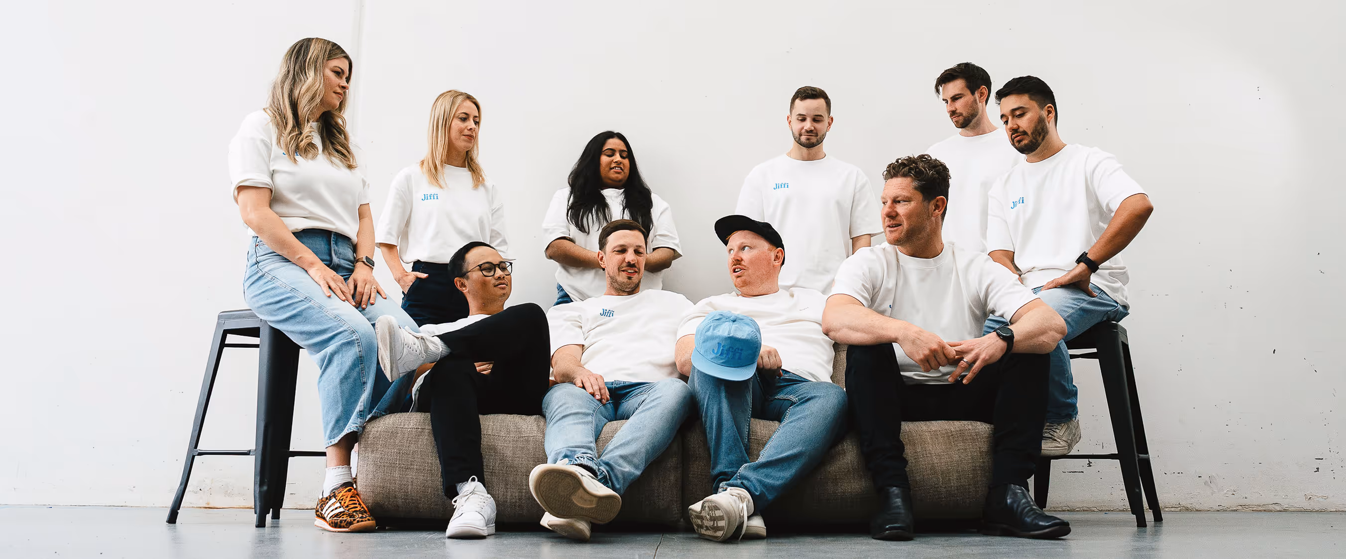 Jiffi team looking at each other, sitting on chairs and a couch with a white background.